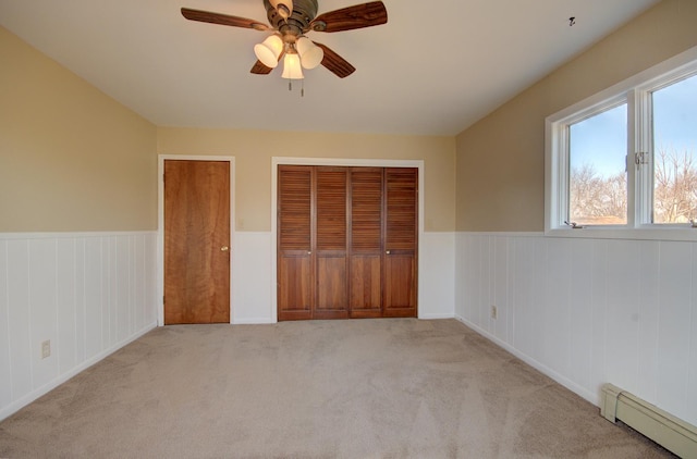 unfurnished bedroom with multiple closets, ceiling fan, light colored carpet, and a baseboard radiator