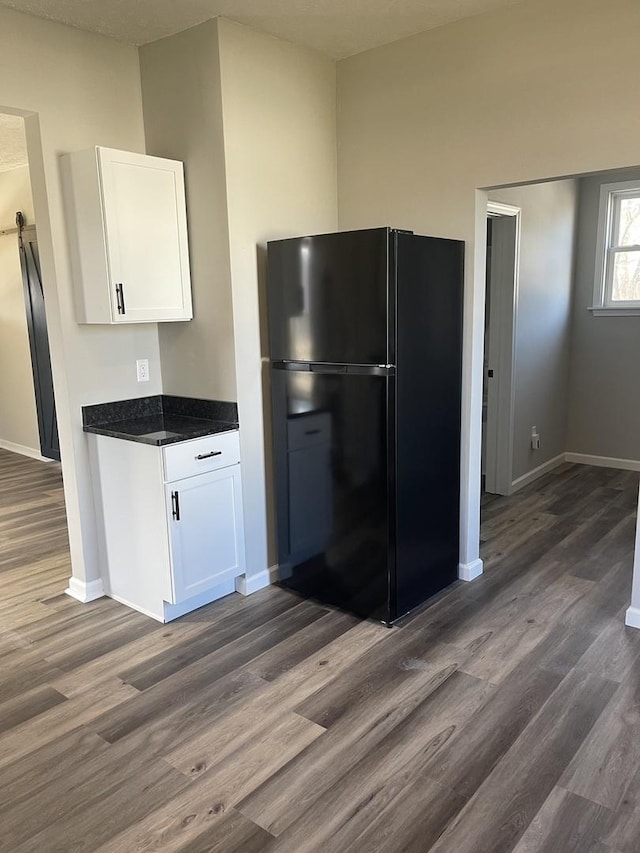 kitchen with white cabinets, black refrigerator, dark hardwood / wood-style flooring, and dark stone counters