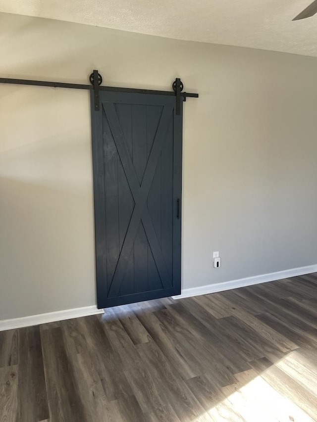 empty room featuring a textured ceiling, a barn door, and dark hardwood / wood-style floors