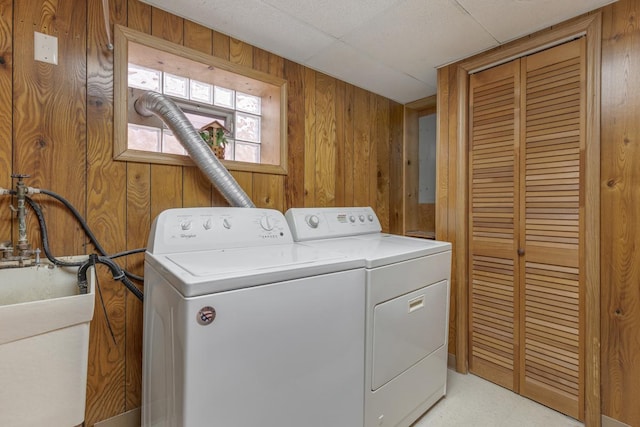 laundry area featuring washer and clothes dryer, wood walls, and sink