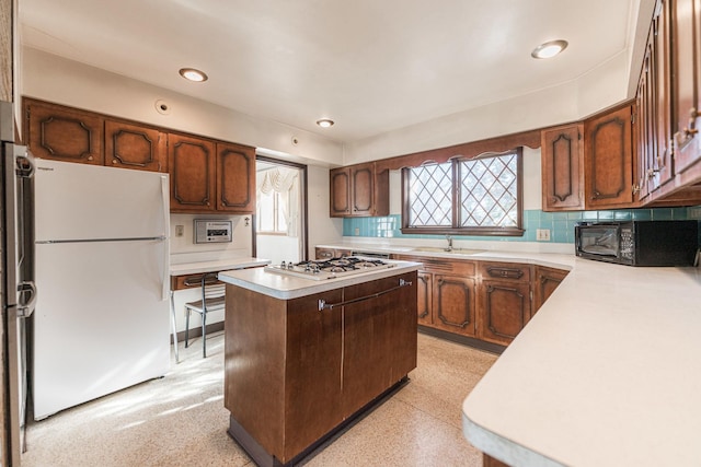 kitchen with gas stovetop, white refrigerator, a kitchen island, sink, and backsplash