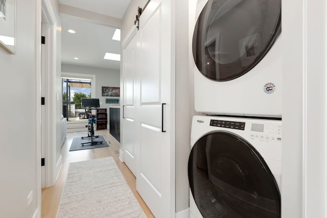 washroom featuring a barn door, light hardwood / wood-style floors, and stacked washer and clothes dryer