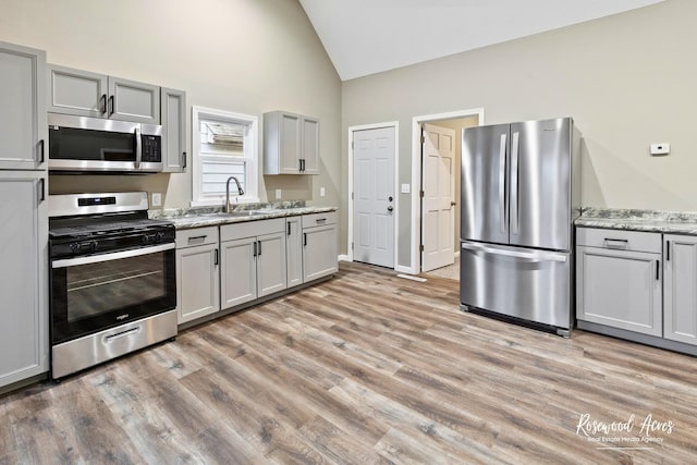 kitchen featuring sink, light stone counters, light hardwood / wood-style floors, gray cabinets, and appliances with stainless steel finishes