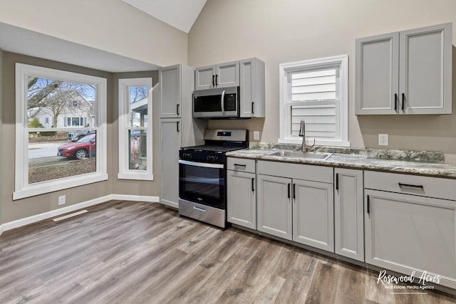 kitchen featuring gray cabinetry, stainless steel appliances, sink, light hardwood / wood-style flooring, and lofted ceiling