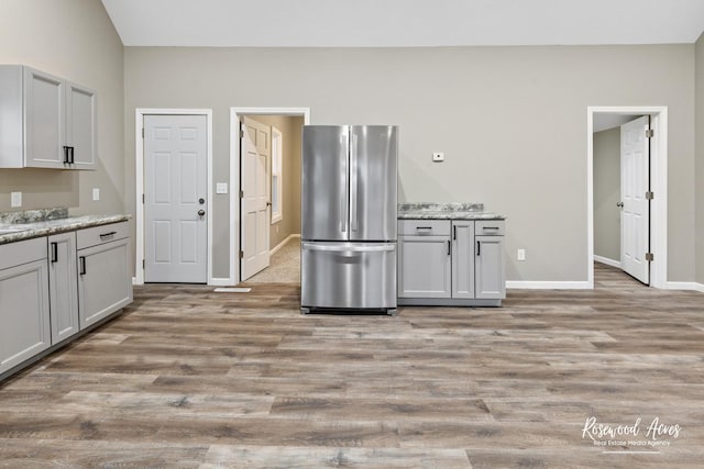 kitchen featuring gray cabinetry, stainless steel fridge, light stone counters, and light hardwood / wood-style flooring