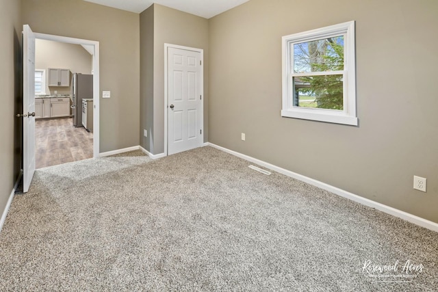 unfurnished bedroom with light carpet and stainless steel refrigerator