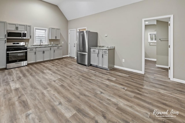 kitchen featuring appliances with stainless steel finishes, light wood-type flooring, gray cabinetry, vaulted ceiling, and sink