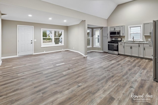 unfurnished living room with high vaulted ceiling, light hardwood / wood-style flooring, and sink