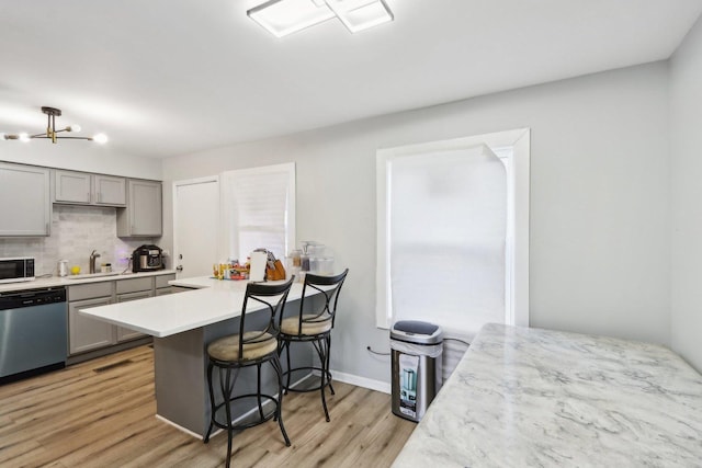 kitchen featuring gray cabinetry, dishwasher, backsplash, a breakfast bar, and light wood-type flooring