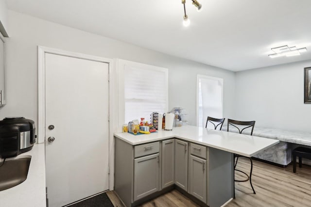 kitchen featuring a breakfast bar area, kitchen peninsula, light hardwood / wood-style flooring, and gray cabinets