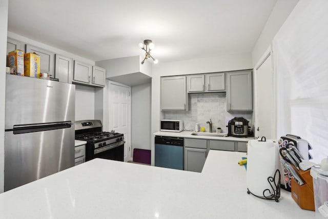 kitchen featuring backsplash, sink, gray cabinets, a notable chandelier, and stainless steel appliances