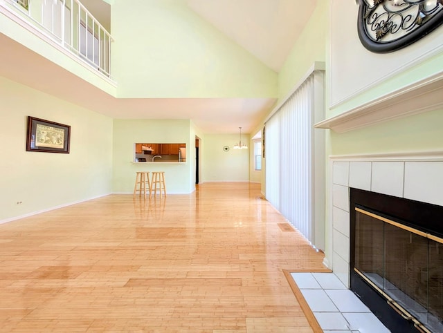 unfurnished living room with a tile fireplace, high vaulted ceiling, and light hardwood / wood-style flooring