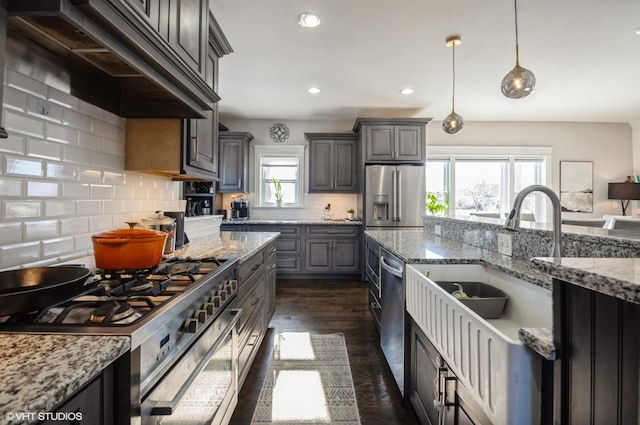 kitchen with stainless steel appliances, premium range hood, light stone counters, sink, and decorative light fixtures