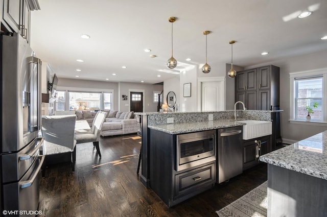 kitchen with a kitchen breakfast bar, a kitchen island with sink, appliances with stainless steel finishes, hanging light fixtures, and sink