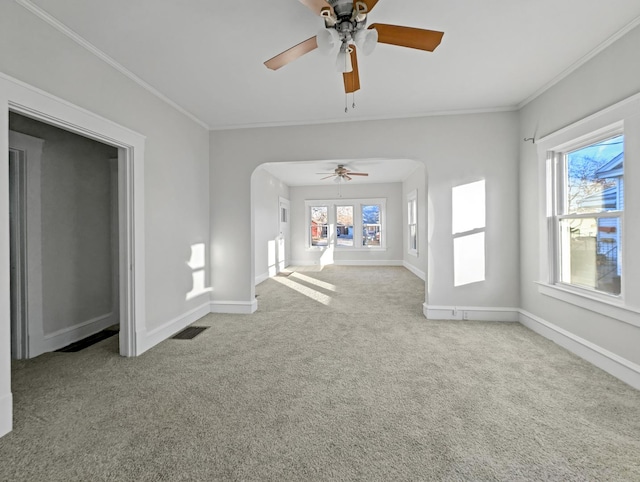 unfurnished living room featuring light carpet, crown molding, ceiling fan, and a healthy amount of sunlight