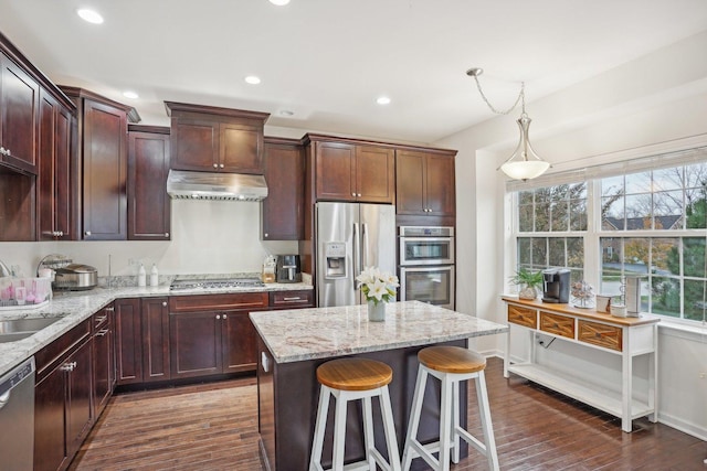 kitchen featuring pendant lighting, a center island, light stone countertops, dark hardwood / wood-style flooring, and stainless steel appliances