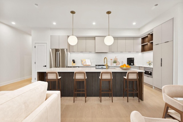 kitchen with a center island with sink, high end fridge, gray cabinetry, and a breakfast bar