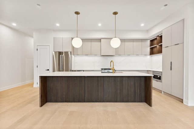 kitchen with sink, hanging light fixtures, a center island with sink, stainless steel refrigerator, and decorative backsplash