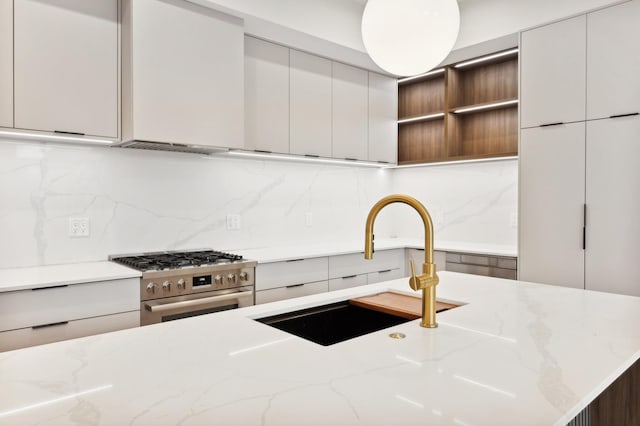 kitchen with light stone countertops, stainless steel range with gas cooktop, sink, and decorative backsplash