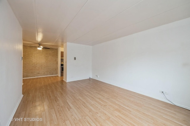 unfurnished room featuring light wood-type flooring, ceiling fan, and brick wall