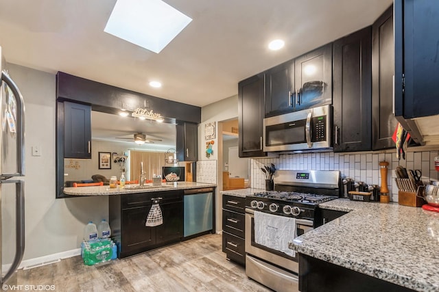 kitchen with light stone countertops, appliances with stainless steel finishes, light wood-type flooring, backsplash, and sink