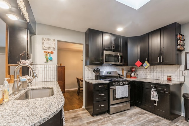 kitchen with sink, light stone countertops, appliances with stainless steel finishes, tasteful backsplash, and light hardwood / wood-style floors