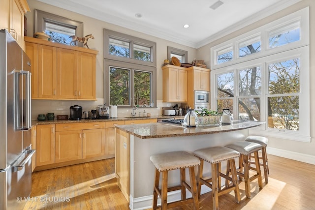 kitchen with a kitchen island, sink, ornamental molding, light stone counters, and stainless steel appliances