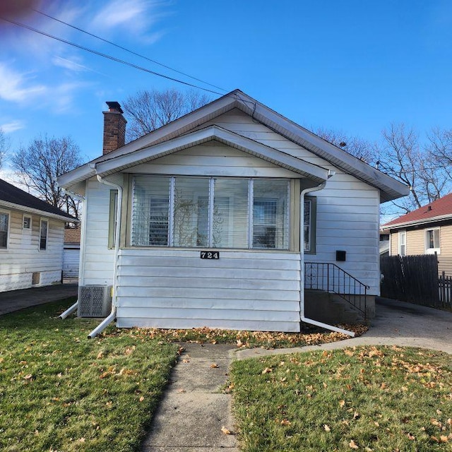 bungalow-style home with a sunroom, central air condition unit, and a front lawn