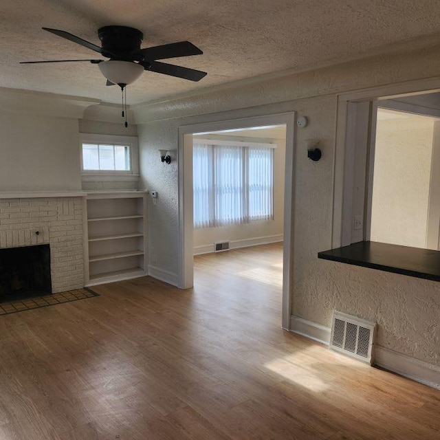 unfurnished living room with a textured ceiling, light hardwood / wood-style floors, a brick fireplace, and ceiling fan