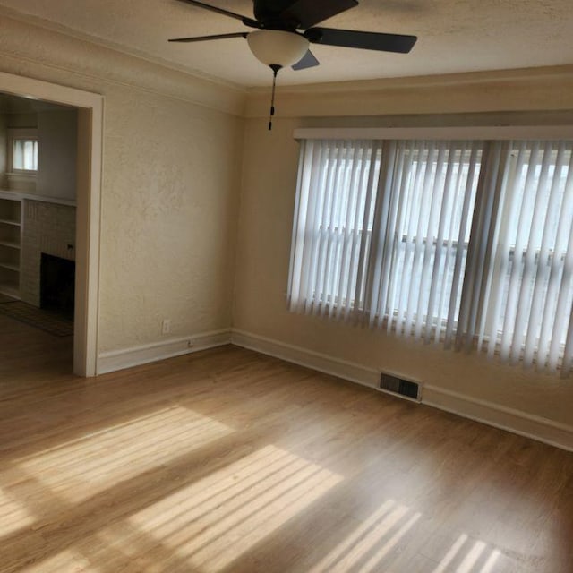 spare room featuring ceiling fan, light hardwood / wood-style floors, ornamental molding, and a fireplace