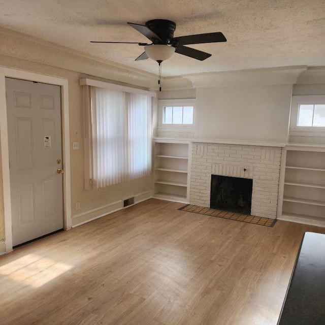 unfurnished living room featuring wood-type flooring, a textured ceiling, a wealth of natural light, and a brick fireplace