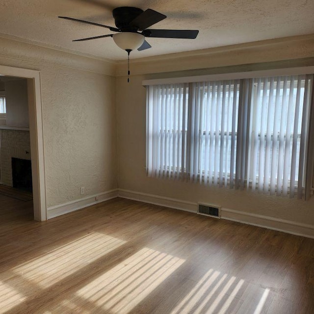 empty room with hardwood / wood-style flooring, a brick fireplace, plenty of natural light, and ceiling fan