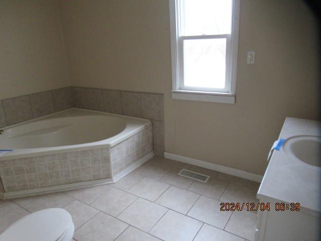 bathroom with tile patterned floors, tiled tub, vanity, and toilet