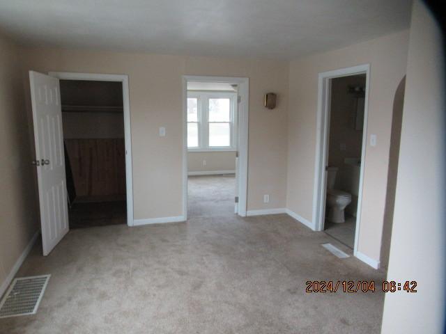 unfurnished bedroom with ensuite bathroom, a spacious closet, light carpet, and a closet