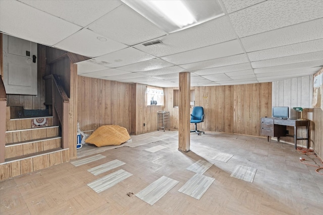 basement featuring a drop ceiling and wooden walls