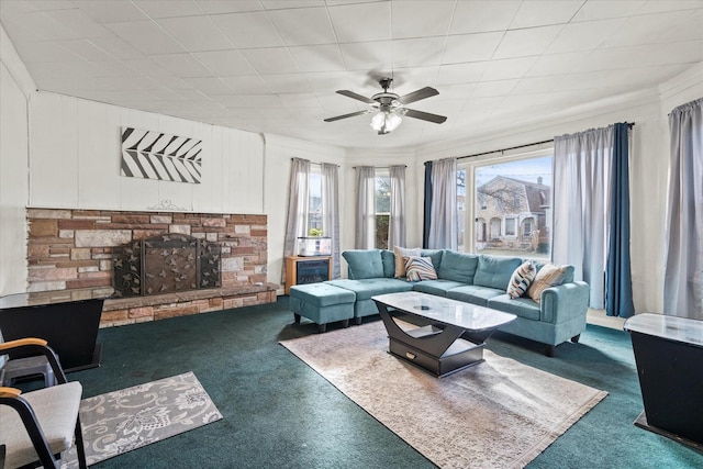 living room with dark carpet, a stone fireplace, ceiling fan, and crown molding