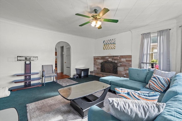 carpeted living room featuring ceiling fan, a stone fireplace, and ornamental molding