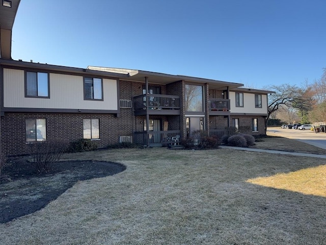 exterior space with brick siding, a balcony, and a lawn