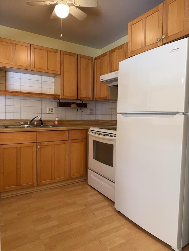 kitchen featuring a sink, under cabinet range hood, tasteful backsplash, white appliances, and light wood-style floors