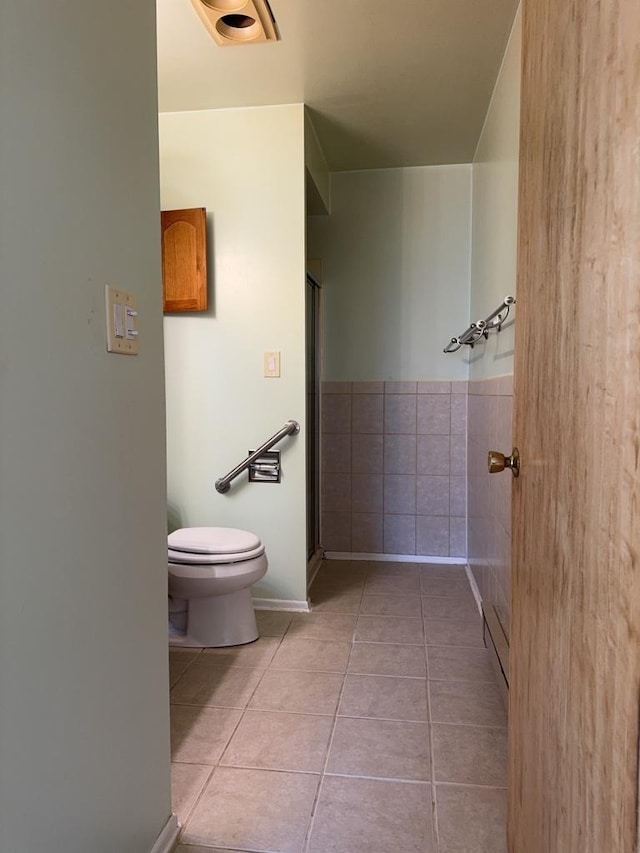 bathroom with tile patterned flooring, a shower stall, toilet, wainscoting, and tile walls