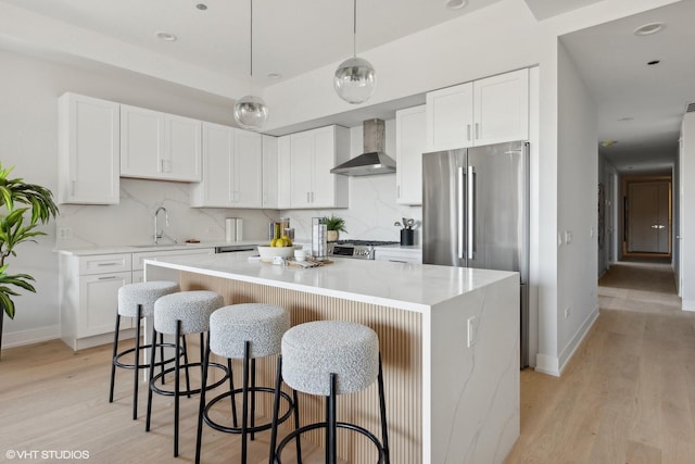 kitchen with white cabinets, a kitchen island, pendant lighting, and wall chimney range hood