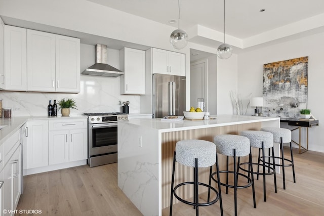 kitchen with appliances with stainless steel finishes, wall chimney exhaust hood, a kitchen island, pendant lighting, and white cabinetry