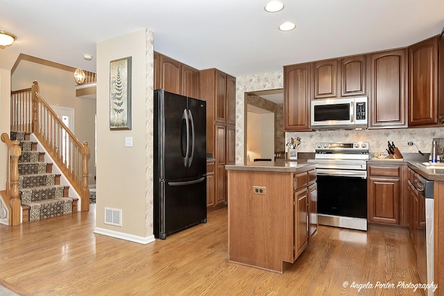 kitchen featuring appliances with stainless steel finishes, backsplash, sink, light hardwood / wood-style floors, and a kitchen island