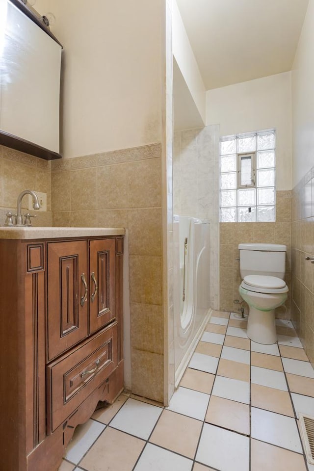 bathroom with tile patterned flooring, vanity, toilet, and tile walls