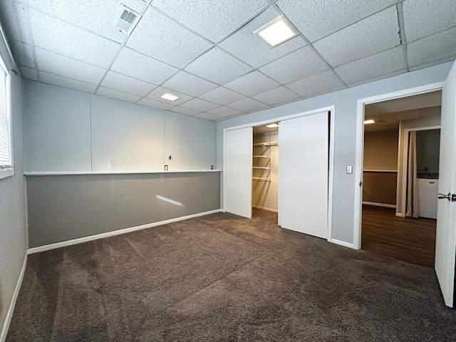 unfurnished bedroom featuring a paneled ceiling, a spacious closet, a closet, and dark colored carpet