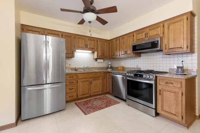 kitchen featuring ceiling fan, sink, stainless steel appliances, light stone counters, and decorative backsplash