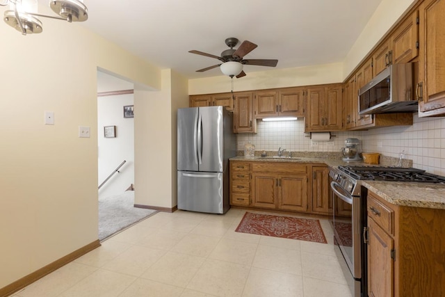 kitchen featuring ceiling fan, sink, light stone counters, decorative backsplash, and appliances with stainless steel finishes