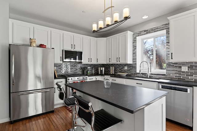 kitchen with appliances with stainless steel finishes, white cabinets, a kitchen island, sink, and hanging light fixtures