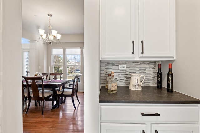 bar with backsplash, hanging light fixtures, white cabinets, and a notable chandelier