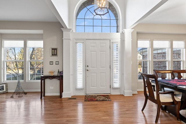 foyer with wood-type flooring, an inviting chandelier, and decorative columns